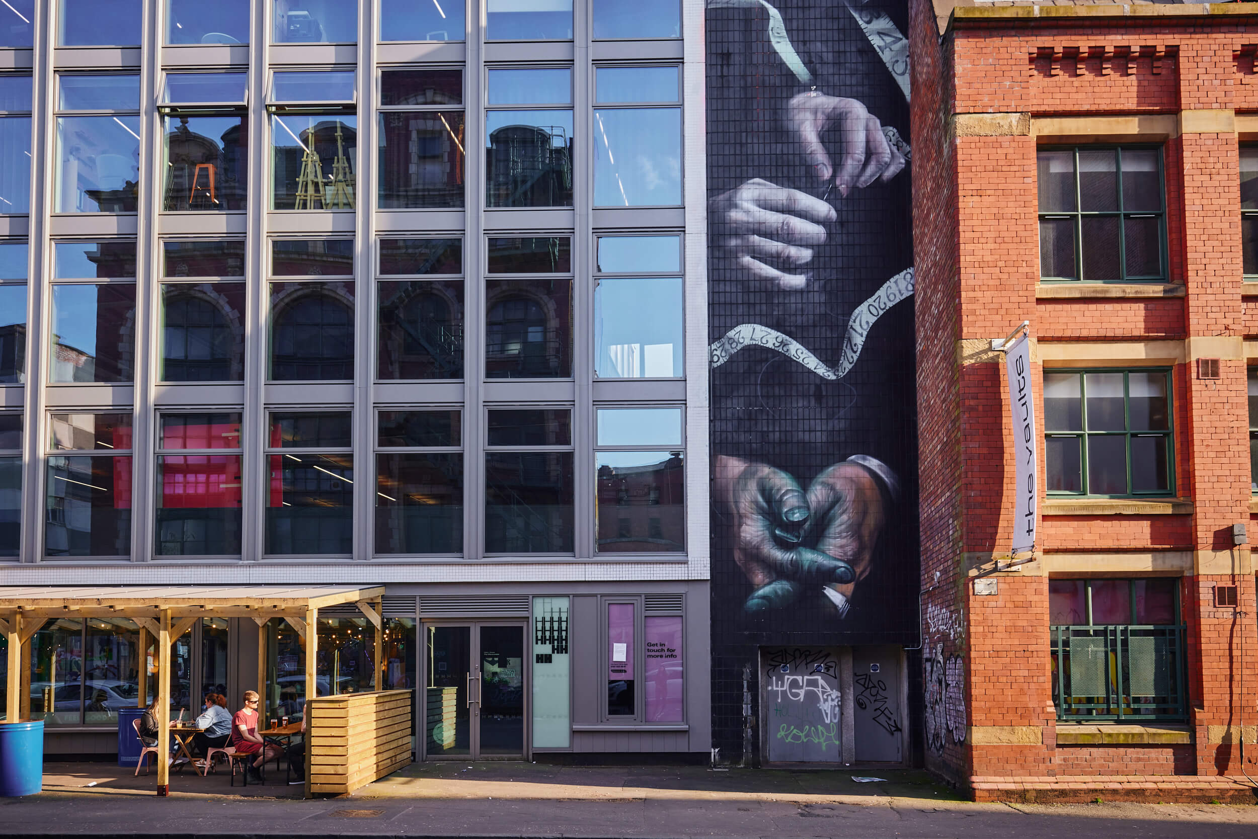 External seating area at Feel Good Club and mural of hands on the side of Hilton House
