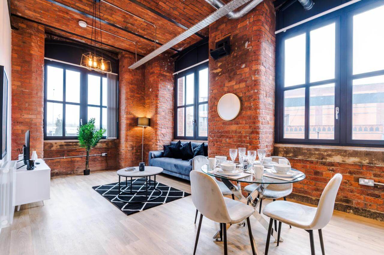 Meadow Mill Stockport exposed brickwork lounge area with coffee table in the middle atop a black and white rug and dining table in the foreground